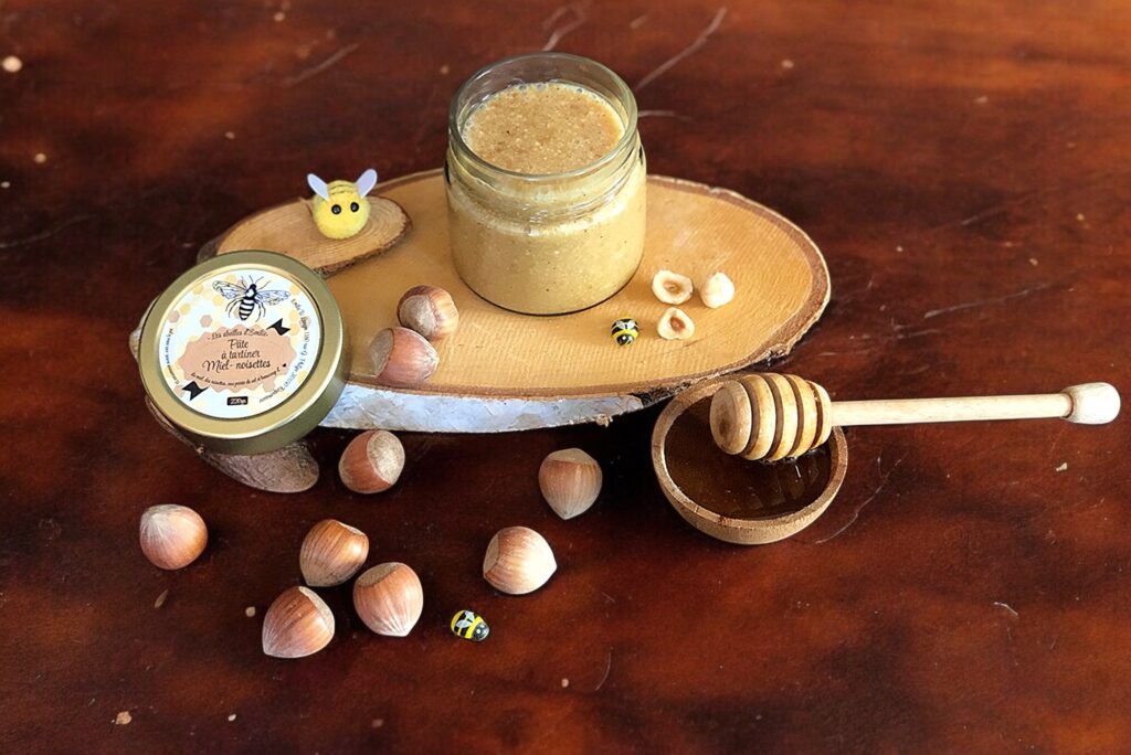 Pâte à tartiner artisanale Les abeilles d'Emilie dans une ambiance chaleureuse (bois, noisettes, miel, cuillère à miel, lumière dorée, texture fondante)