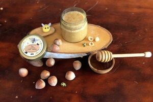 Photo de pâte à tartiner miel noisettes dans une ambiance chaleureuse et artisanale (bois, noisettes, miel, lumière dorée, texture fondante)